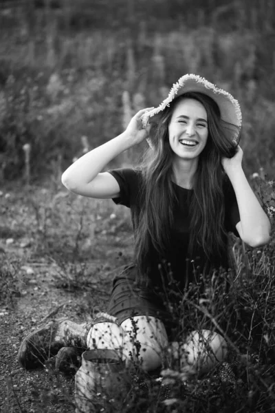 花の近くに座って彼女の頭の上に帽子と長い髪の少女の黒と白の写真 彼女は田舎を散歩に行った — ストック写真
