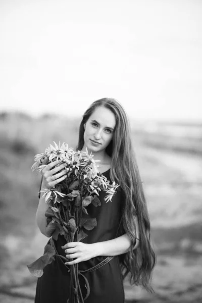野の花の花束を集めている長い髪を持つ美しい少女の黒と白の写真 田舎を歩きなさい 女の子とともにA花束のデイジー — ストック写真