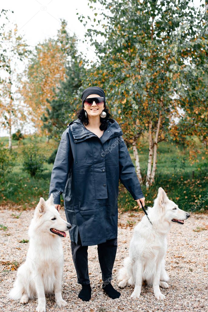 A girl in a jacket and black glasses leads two white dogs on leashes. Big beautiful white dogs. girl walks the dogs.