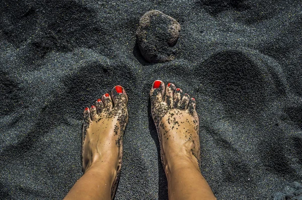 Weibliche nackte Füße mit roten Nägeln am schwarzen Sandstrand — Stockfoto