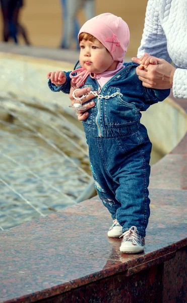 Little girl makes the first steps with his mother near the fountain — Stock Photo, Image