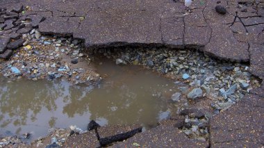 Yolun su erozyonu. Kırık asfalt arka plan. Tehlike deliği, taştan gri zemin
