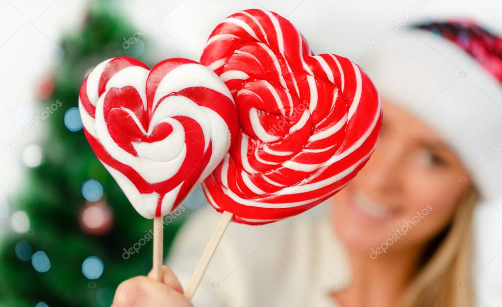 Blurred portrait of smiling woman holding two candies in a heart shape. Christmas holiday