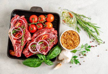 Taze çiğ biftek, hardal tohumları, baharatlı yağ, bitkiler ve gri beton arka planda sebzeler. Düz uzanın, başınızın üstünde