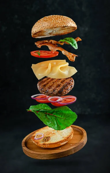 Flying hamburger with ingredients on dark stone background. Creative still life