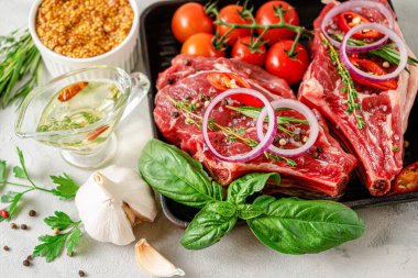 Taze çiğ biftek, hardal tohumları, baharatlı yağ, bitkiler ve gri beton arka planda sebzeler. Seçici odak