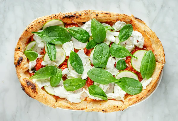 Roman pizza with spinach, zucchini slices, stracciatella cheese and tomatoes on marble background.. Italian food, overhead