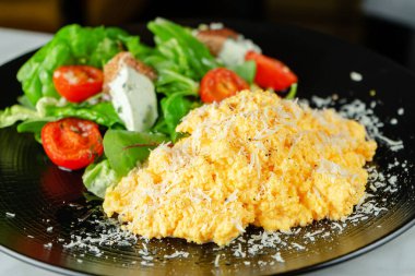 Çırpılmış yumurtayı siyah tabakta salatayla kapat. Kahvaltı yemeği..