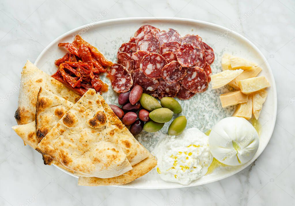 Antipasto platter with different cheese, meat and focaccia on marble background. Italian snack