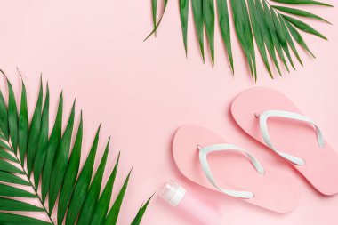 Palmiye yaprağı, terlik ve pastel pembe arka planda güneş kremi şişesi. Yukarıdan, boşluğu kopyala.