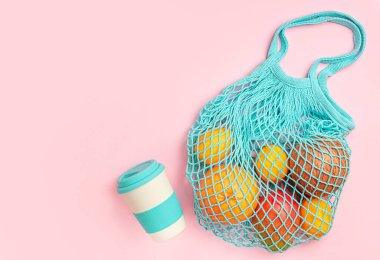 Yeniden kullanılabilir eko torba içinde çeşitli meyveler ve pembe arka planda bambu kapları. Üst görünüm, alanı kopyala.