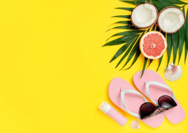 Plaj aksesuarları ve parlak sarı arka planda güneş kremi şişesi. Düz yat, boşluğu kopyala.