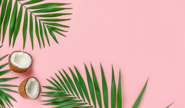 Pembe arka planda palmiye yaprakları olan iki hindistan cevizi yarım. Düz yat, boşluğu kopyala.