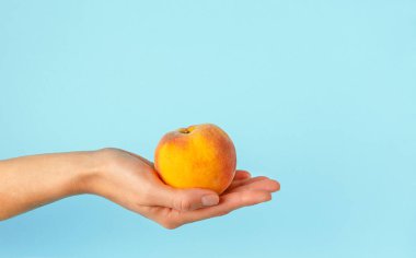 Mavi arka planda şeftali tutan bir kadın. Boşluğu kopyala