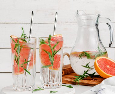 Beyaz ahşap arka planda grepefruit ve biberiyeli sağlıklı narenciye içeceği. Erimiş su.