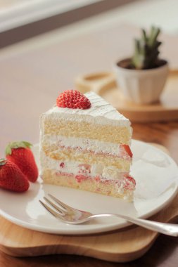 Çilekli keki yakın plan beyaz bir tabakta, çatal ve dekorasyon meyveli kremalı servis, kafedeki Tahta Masada Tatlı Yemeği