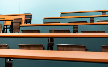 Üniversite ders sınıfında ahşap koltuklu boş öğrenci masası, okul eğitimi geçmişi.