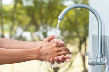 Adam musluk musluğu ile çalıştıktan sonra elini yıkıyor, akan su ve yeşil orman arka planıyla hijyen koruma kavramını temizliyor.