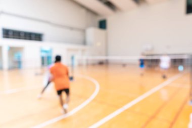 İkili takımlarda badminton oynayan insanlar jimnastik kortunda oynuyorlar.