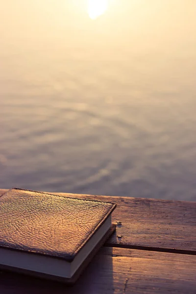 Notebook on the wooden Table with bokeh Sunset background of Lake, Relax Holiday Time in the Park, Happy Learning Concept