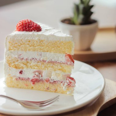 Çilekli keki yakın plan beyaz bir tabakta, çatal ve dekorasyon meyveli kremalı servis, kafedeki Tahta Masada Tatlı Yemeği