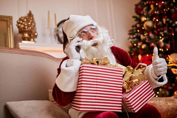 Święty Mikołaj Siedzi Kanapie Rozmawia Przez Telefon Komórkowy Pobliżu Kominka — Zdjęcie stockowe