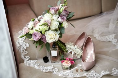 Ayakkabı, buket, yüzük ve parfüm gibi düğün aksesuarları bir masanın üzerinde bulunur.