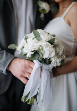 Gelin ve damat ellerinde kurdele detaylarıyla birlikte beyaz buket tutuyorlar. Yüksek kalite fotoğraf