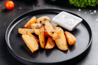 Kremalı otlu siyah tabağa batırılmış çıtır patates dilimleri, yakın çekim. Yüksek kalite fotoğraf