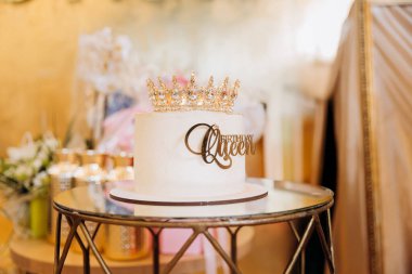 Beyaz doğum günü pastası, üzerinde altın taç süsü ve zarif bir partide doğum günü kraliçesi işareti var. Yüksek kalite fotoğraf