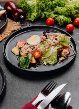 Yumurtalı ton balığı salatası, siyah tabakta domates ve yeşillikler, restoranın öğle yemeği yakın çekimi. Yüksek kalite fotoğraf