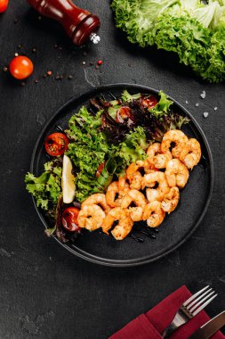 Karışık sebzeli ızgara karides salatası, vişneli domates ve siyah tabakta limon. Yüksek kalite fotoğraf