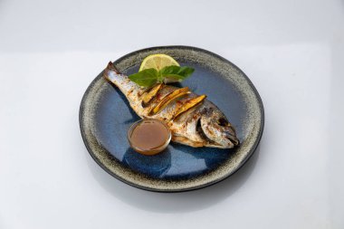 Mavi seramik tabakta limon, fesleğen ve soslu ızgara dorado, beyaz arka plan. Yüksek kalite fotoğraf