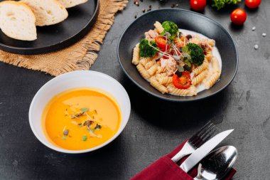 Ton balığı, brokoli ve vişneli domatesli kremalı fusilli, karanlık masada çorba ile servis ediliyor. Yüksek kalite fotoğraf