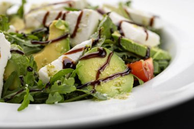 Avokado roka salatasını beyaz tabakta feta ve balzamik cila ile kapat. Yüksek kalite fotoğraf