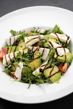 Avokado roka salatasını beyaz tabakta feta ve balzamik cila ile kapat. Yüksek kalite fotoğraf