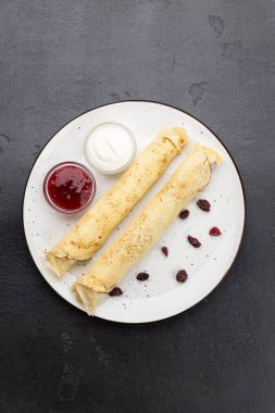 Beyaz tabakta reçelli krep ve ekşi krema, koyu arka planda üst manzara. Yüksek kalite fotoğraf