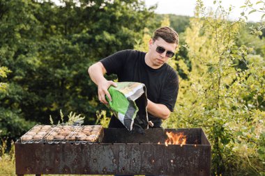 Adam mangal mangalına mangal kömürü döküyor, dışarıda mantar barbeküsü için ateş yakıyor. Yüksek kalite fotoğraf