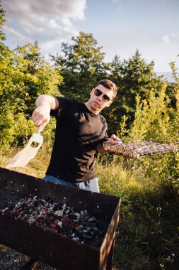 Adam gün batımında dışarıda mangal yapıyor, yaz barbeküsünde kıvılcımlar uçuşuyor. Yüksek kalite fotoğraf