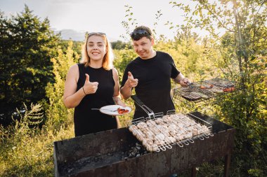Çiftler gün batımında açık havada barbekü yaparken başparmak kaldırıyor. Yüksek kalite fotoğraf