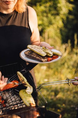 Barbeküden ızgara sebze servis eden bir kadın, yaz güneşinde dışarıda tabağı tutan bir kadın. Yüksek kalite fotoğraf