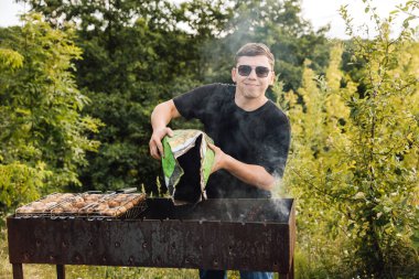 Adam mangal mangalına mangal kömürü döküyor, dışarıda mantar barbeküsü için ateş yakıyor. Yüksek kalite fotoğraf