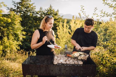 Gün batımında dışarıda sebze ızgara yapan çiftler yaz barbeküsünde yemek tadıyorlar. Yüksek kalite fotoğraf