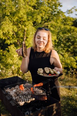 Gülümseyen kadın altın saatinde açık havada ızgara sebze ve tabak tutuyordu. Yüksek kalite fotoğraf