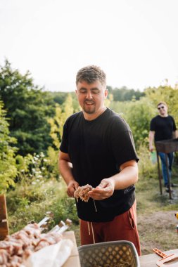 Barbeküden önce dışarıda et şişleri hazırlayan adam gün batımında salamuraya yatırılmış parçaları salamura ediyor. Yüksek kalite fotoğraf
