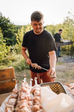 Barbeküden önce dışarıda et şişleri hazırlayan adam gün batımında salamuraya yatırılmış parçaları salamura ediyor. Yüksek kalite fotoğraf