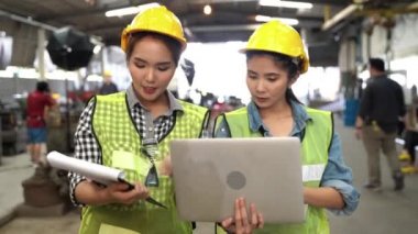 Tablet bilgisayar ve kağıt dosya raporlarıyla yürüyen ve tartışan iki fabrika çalışanı. Endüstriyel fabrikanın arka planında.