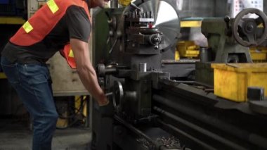 El işçisi, güvenlik üniforması giyen, gözlüklü ve sert şapkalı çelik makineyi kontrol ediyor. Arka planda Odaklanmamış Büyük Endüstriyel Fabrika.