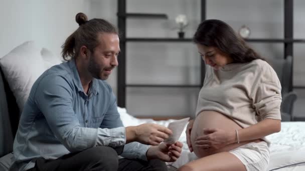 X線映画の赤ちゃんを見ている夫婦の家族です 妊娠中の女性の腹を世話し寝室で妻の腹とキスをする男 産前産後ケアと女性妊娠の概念 — ストック動画