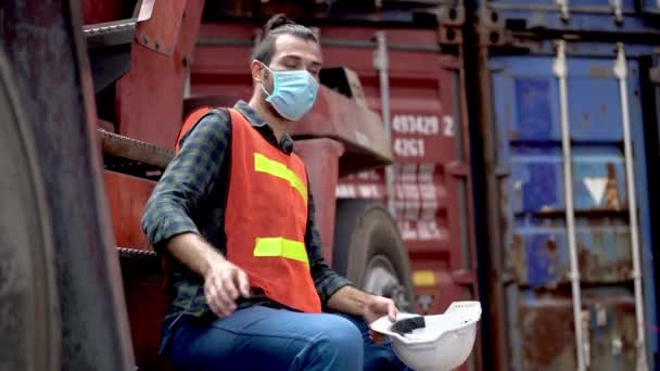 仕事の後リラックスして座っている労働者の男性労働者と機械クレーン屋外倉庫工場で保護マスク顔を離陸します 産業労働者の概念 — ストック動画